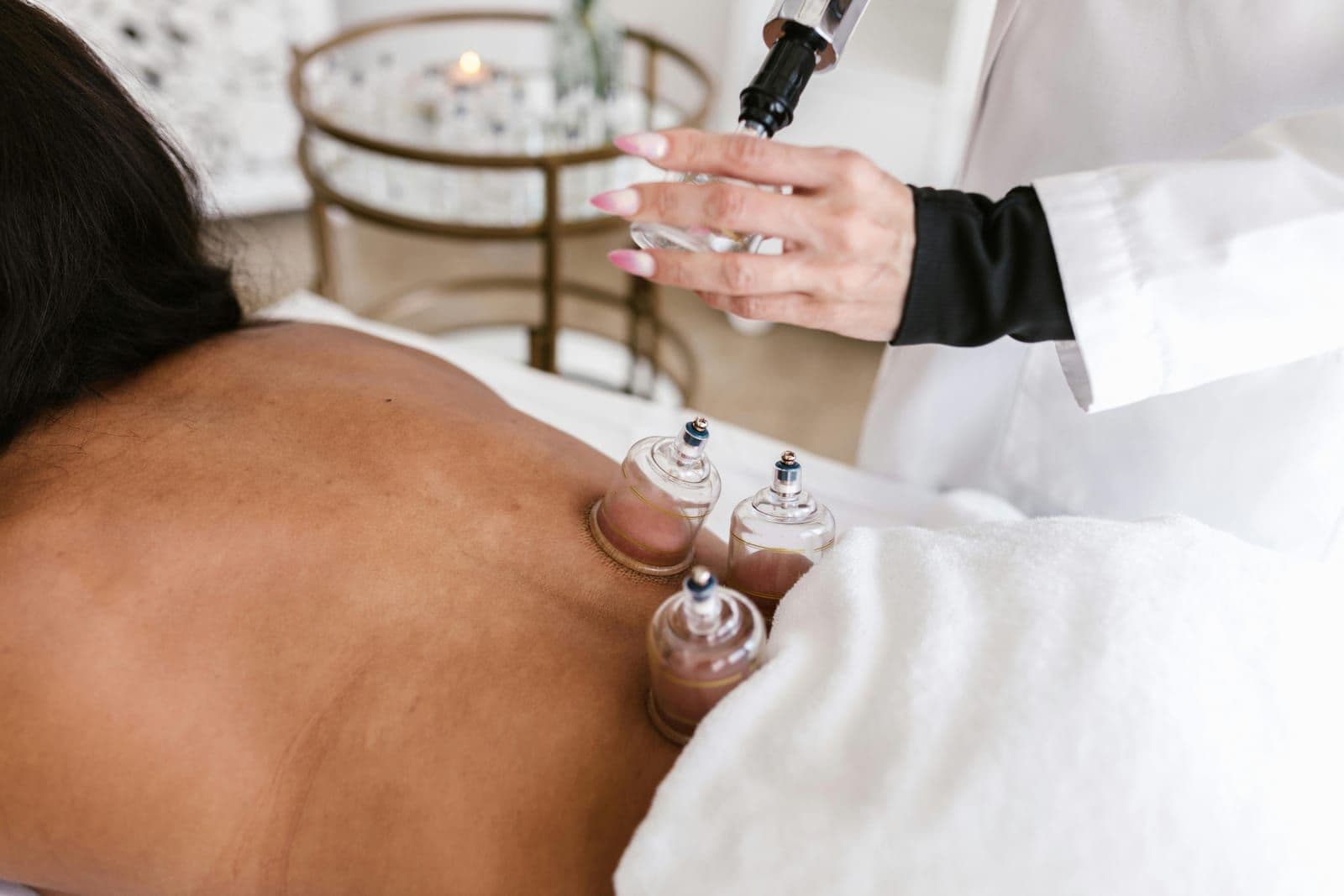 A cupping massage session with glass cups placed on a client's back while a therapist prepares the treatment.